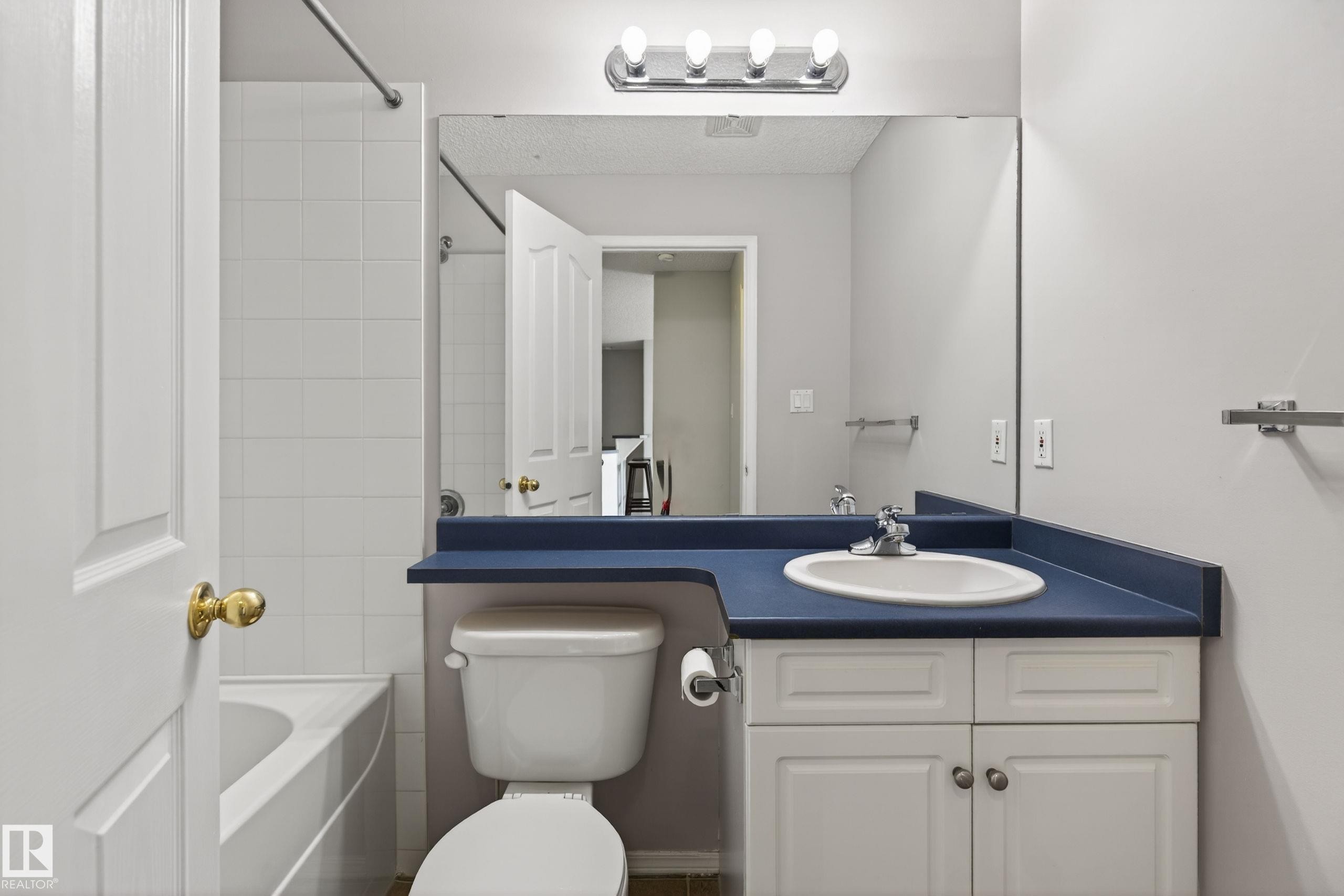 Bathroom featuring a built-in vanity with a dark blue countertop, an undermount sink, and white cabinetry - #319 16303 95 St Nw, Edmonton, AB - Indoor Photo Showing Bathroom