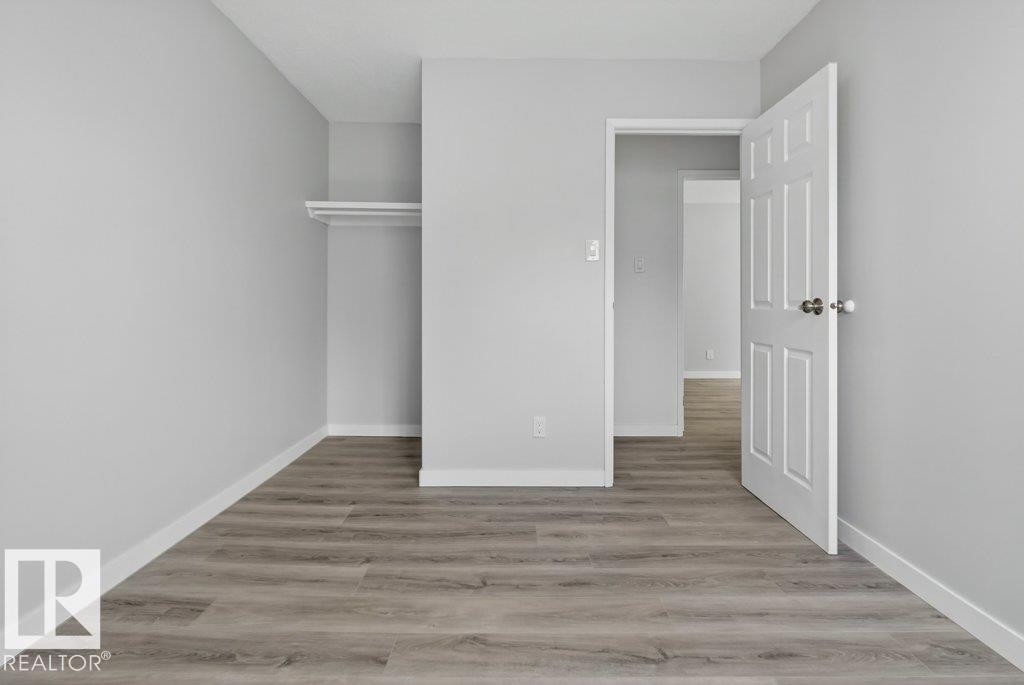 Room featuring wood-finish flooring, light gray walls, white baseboards, and an open closet with shelving and hanging rod - 3E Twin Terrace, Edmonton, AB - Indoor Photo Showing Other Room