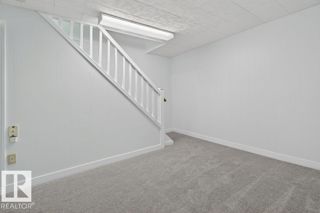 Interior room with light gray carpeting, white vertical paneling, and a white staircase with a matching railing - 3E Twin Terrace, Edmonton, AB - Indoor Photo Showing Other Room