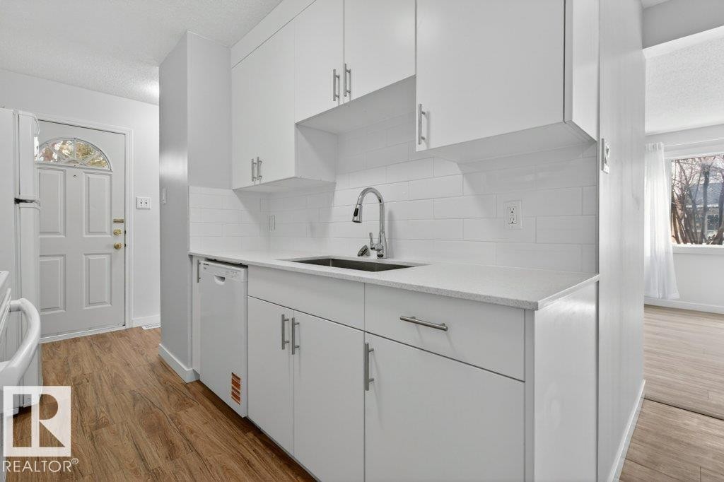 Modern kitchen featuring white shaker cabinetry, light-toned countertops, a stainless steel sink, subway tile backsplash, and wood-finish flooring - 3E Twin Terrace, Edmonton, AB - Indoor Photo Showing Kitchen