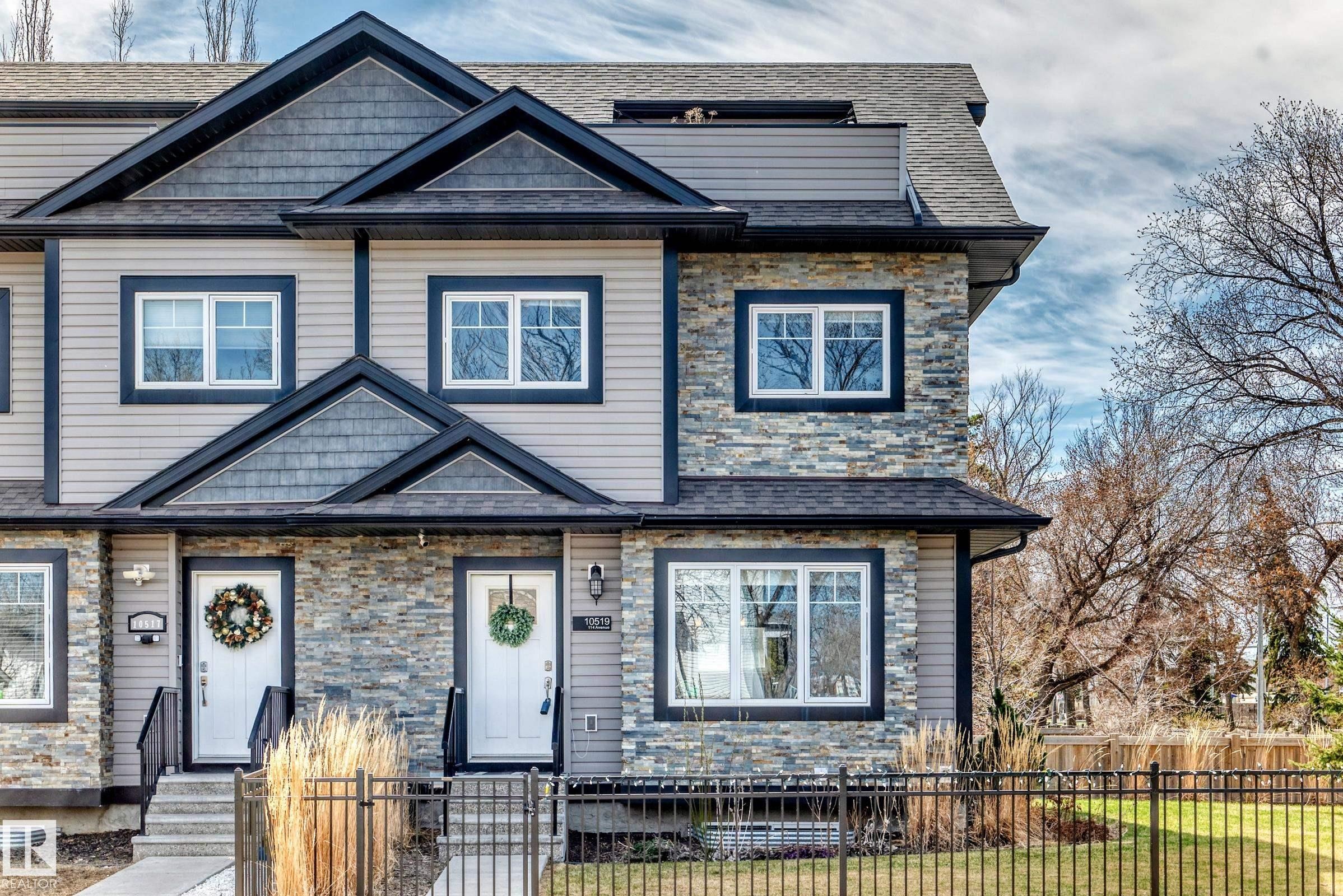Two-story townhome exterior featuring stone and siding finishes, black trim windows, a shingled roof, a front yard with a black metal fence, and a concrete walkway - 10519 114 Avenue, Edmonton, AB - Outdoor With Facade