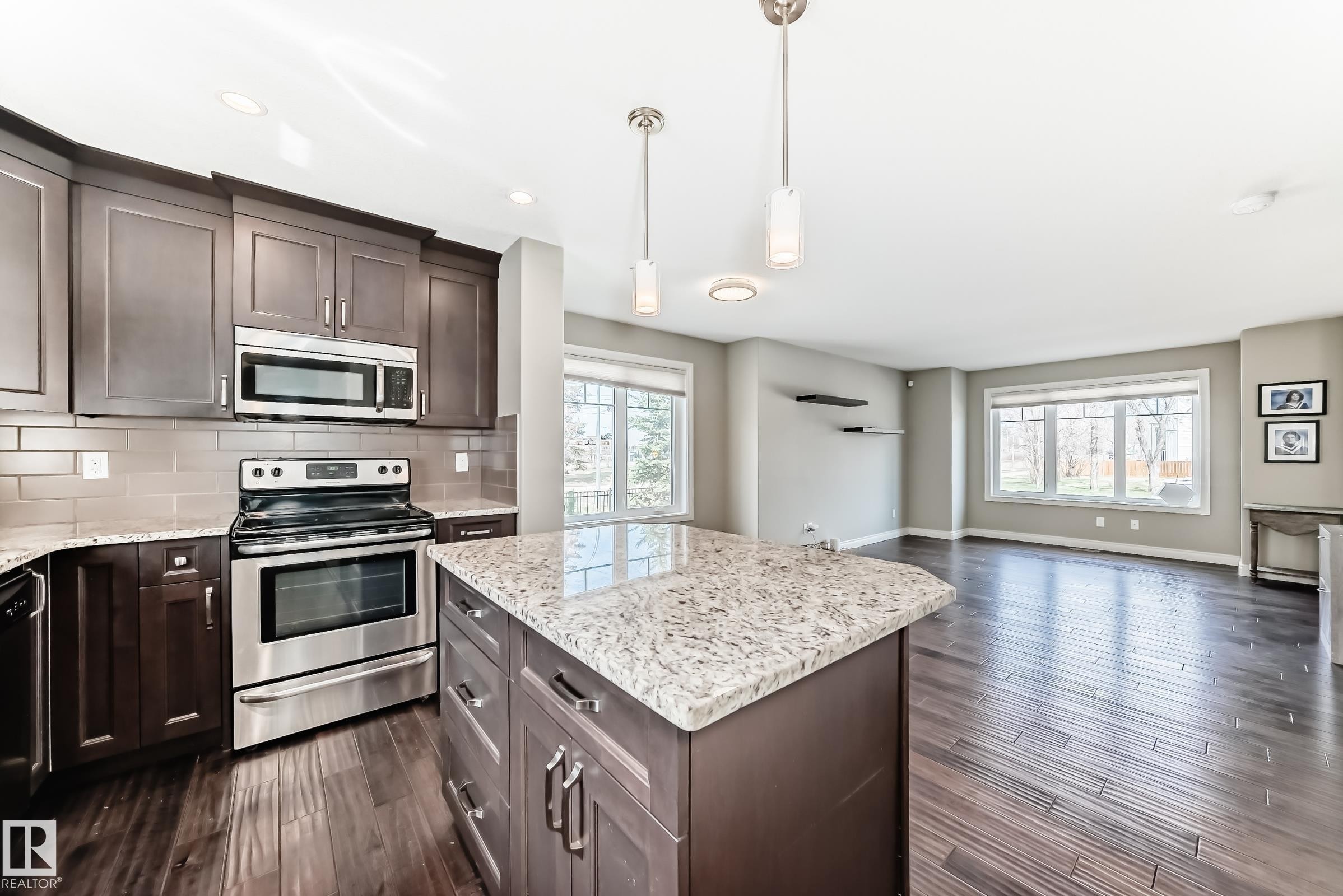 Spacious kitchen featuring dark wood cabinetry, stainless steel appliances, and a central island with a light-toned granite countertop - 10519 114 Avenue, Edmonton, AB - Indoor Photo Showing Kitchen With Stainless Steel Kitchen With Upgraded Kitchen