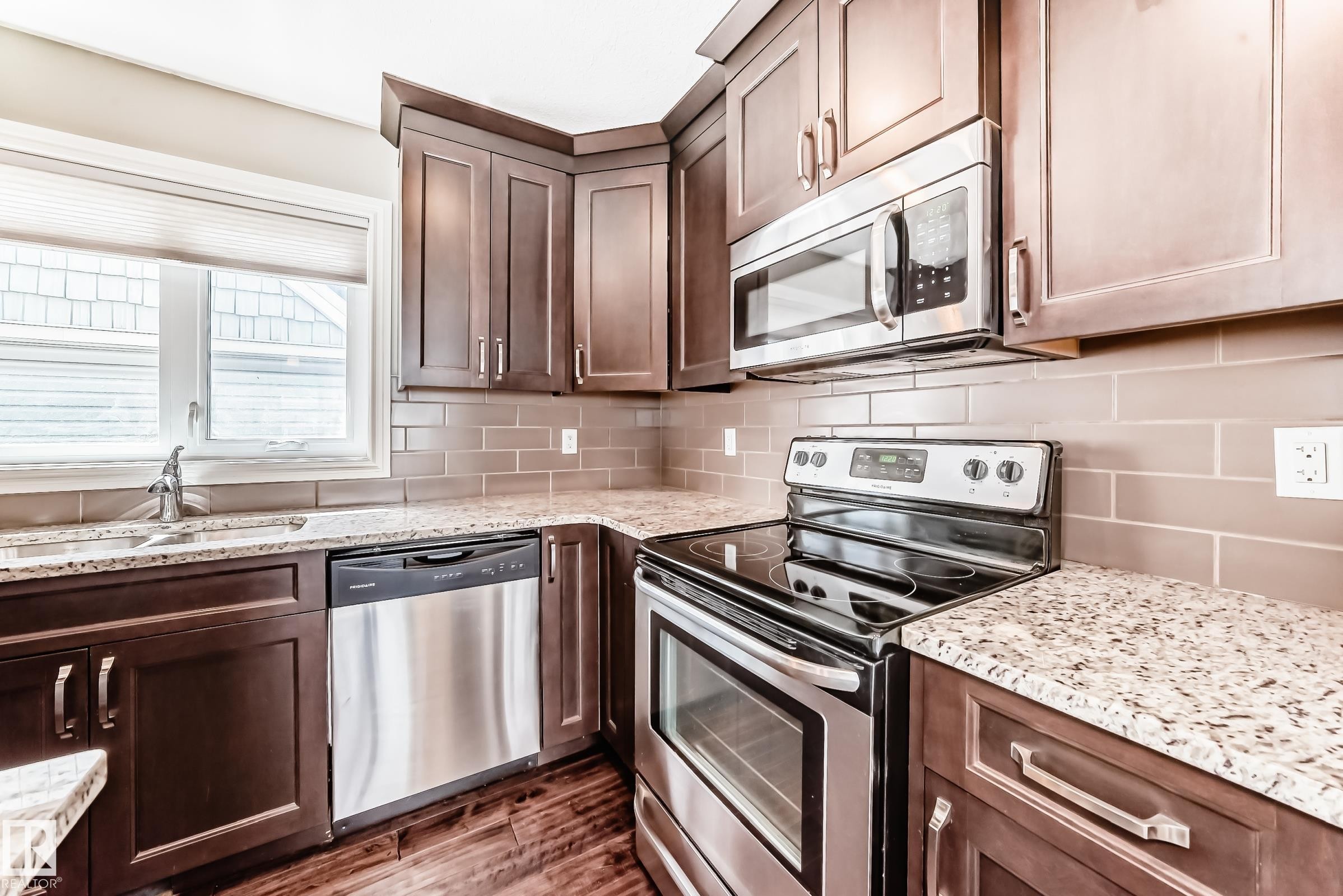 Kitchen featuring wood-finish cabinetry, stainless steel appliances including a built-in microwave, dishwasher, and electric range, granite-style countertops, and a subway tile backsplash - 10519 114 Avenue, Edmonton, AB - Indoor Photo Showing Kitchen With Stainless Steel Kitchen With Upgraded Kitchen