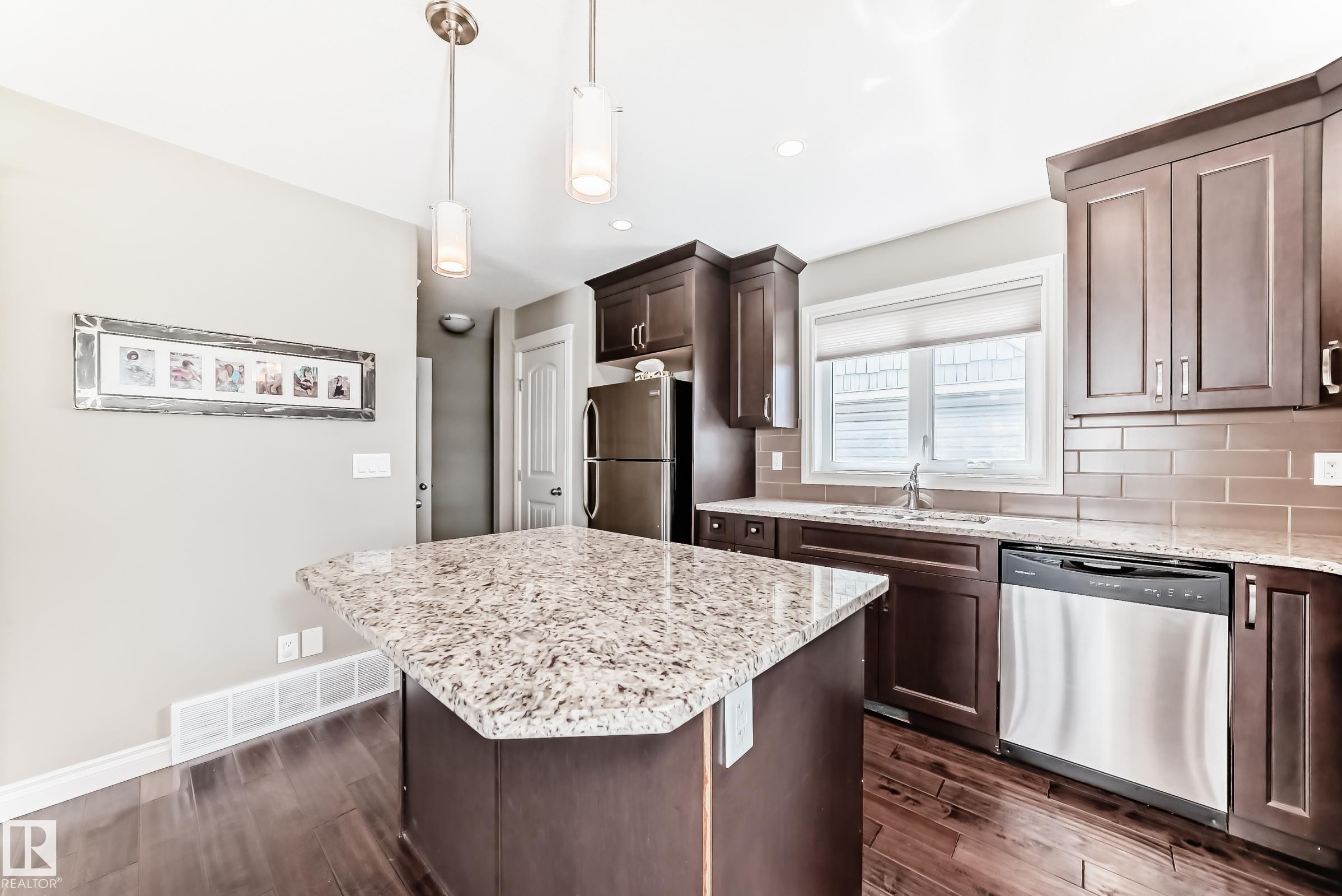 Kitchen featuring an island with a speckled countertop, dark wood-finish cabinetry, stainless steel appliances, and wood-finish flooring - 10519 114 Avenue, Edmonton, AB - Indoor Photo Showing Kitchen With Upgraded Kitchen