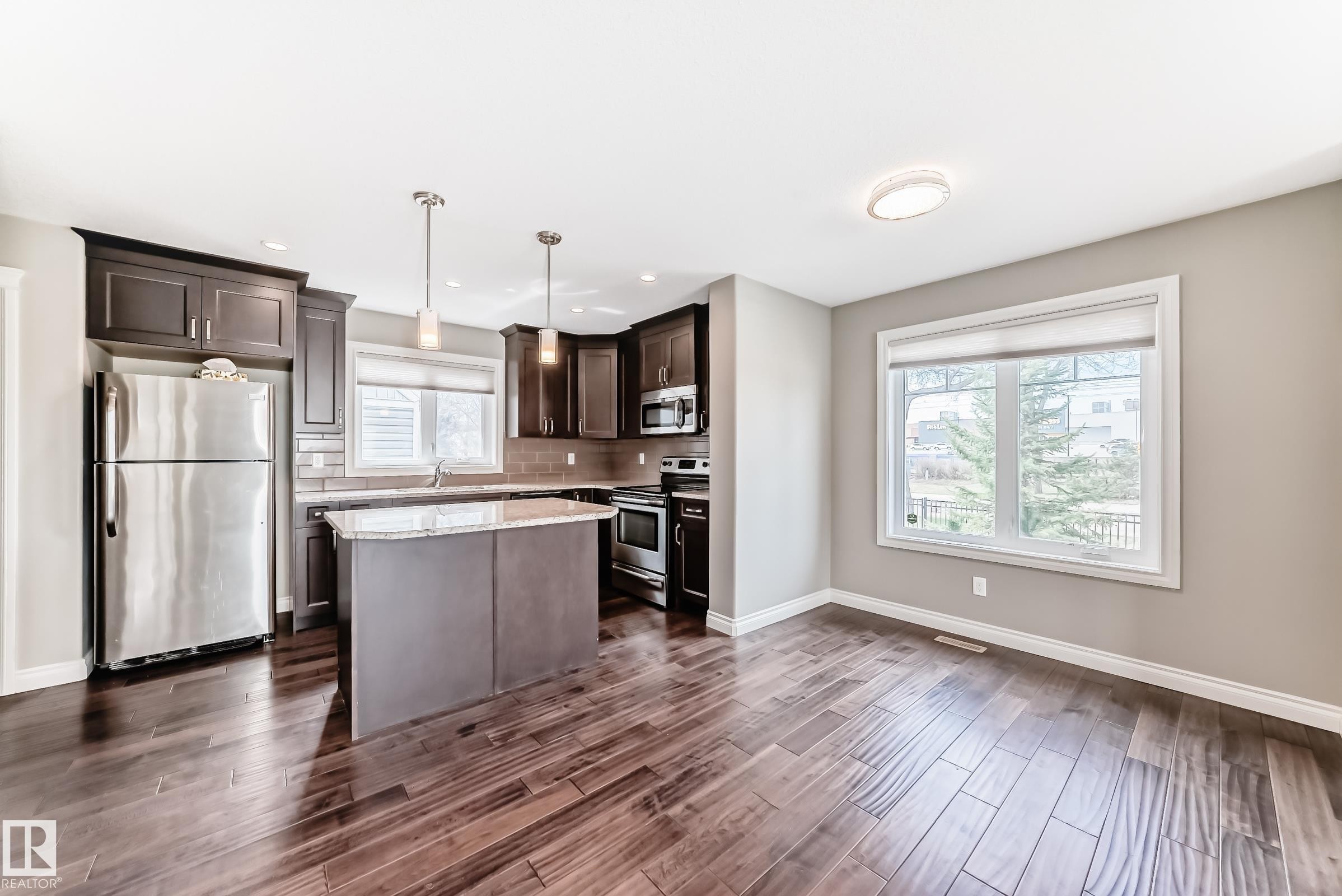 Modern kitchen featuring dark wood cabinetry, stainless steel appliances, a center island with a stone countertop, and wood-finish flooring - 10519 114 Avenue, Edmonton, AB - Indoor Photo Showing Kitchen With Stainless Steel Kitchen With Upgraded Kitchen