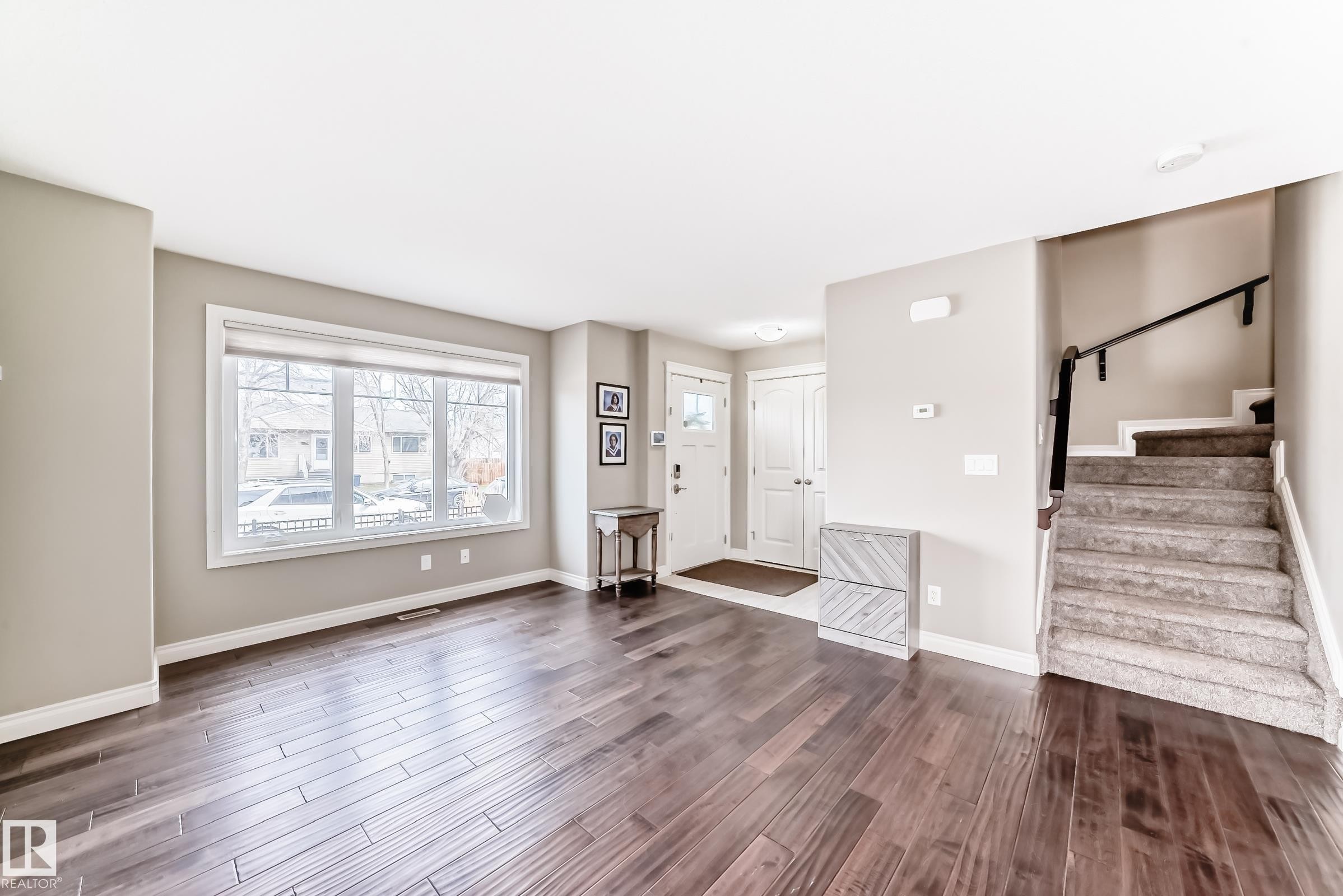 Spacious living area featuring wood-finish flooring, a large picture window with white trim, and neutral wall paint - 10519 114 Avenue, Edmonton, AB - Indoor Photo Showing Other Room