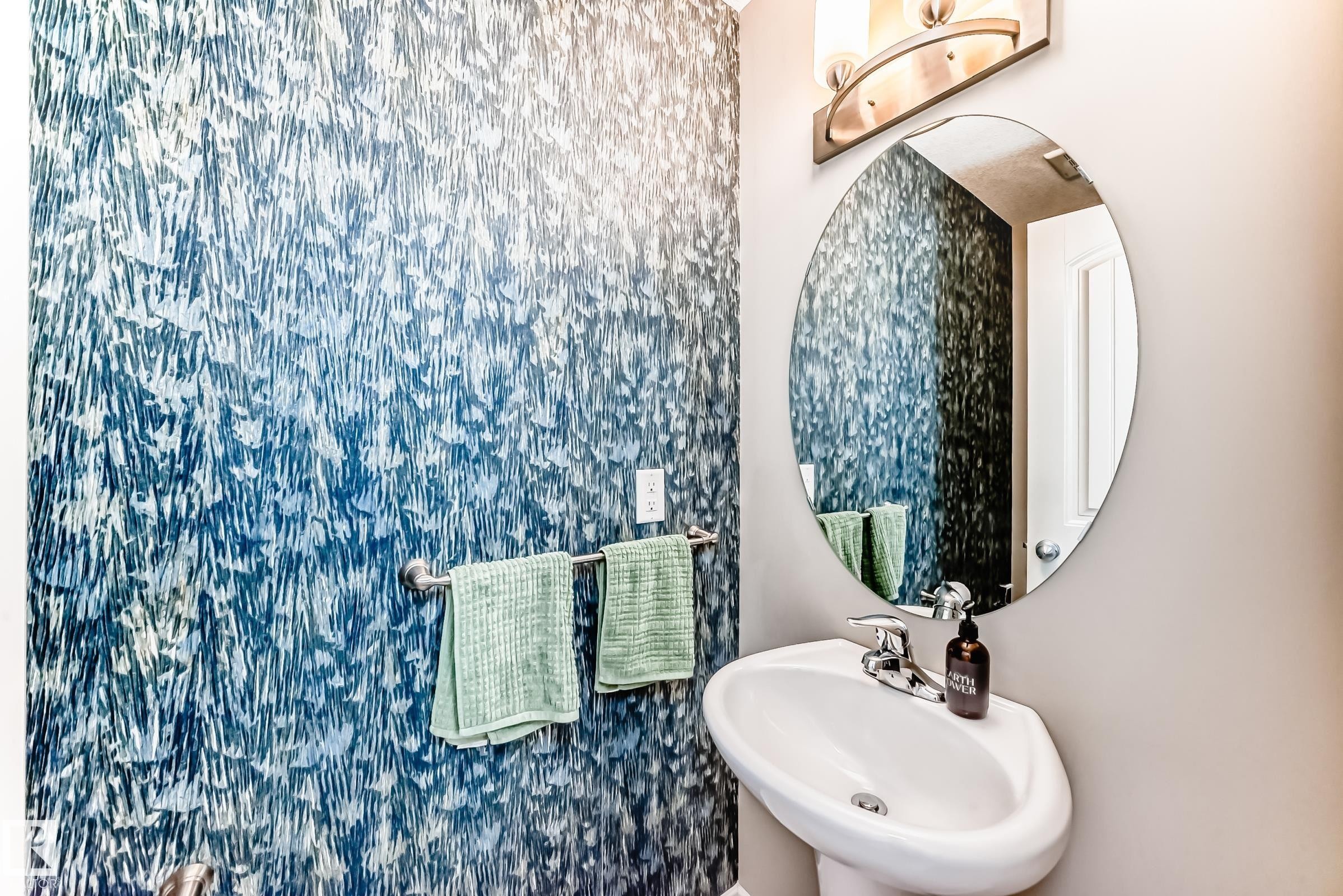 Powder room featuring a pedestal sink with chrome faucet, an oval wall mirror, and a wall-mounted light fixture - 10519 114 Avenue, Edmonton, AB - Indoor Photo Showing Bathroom