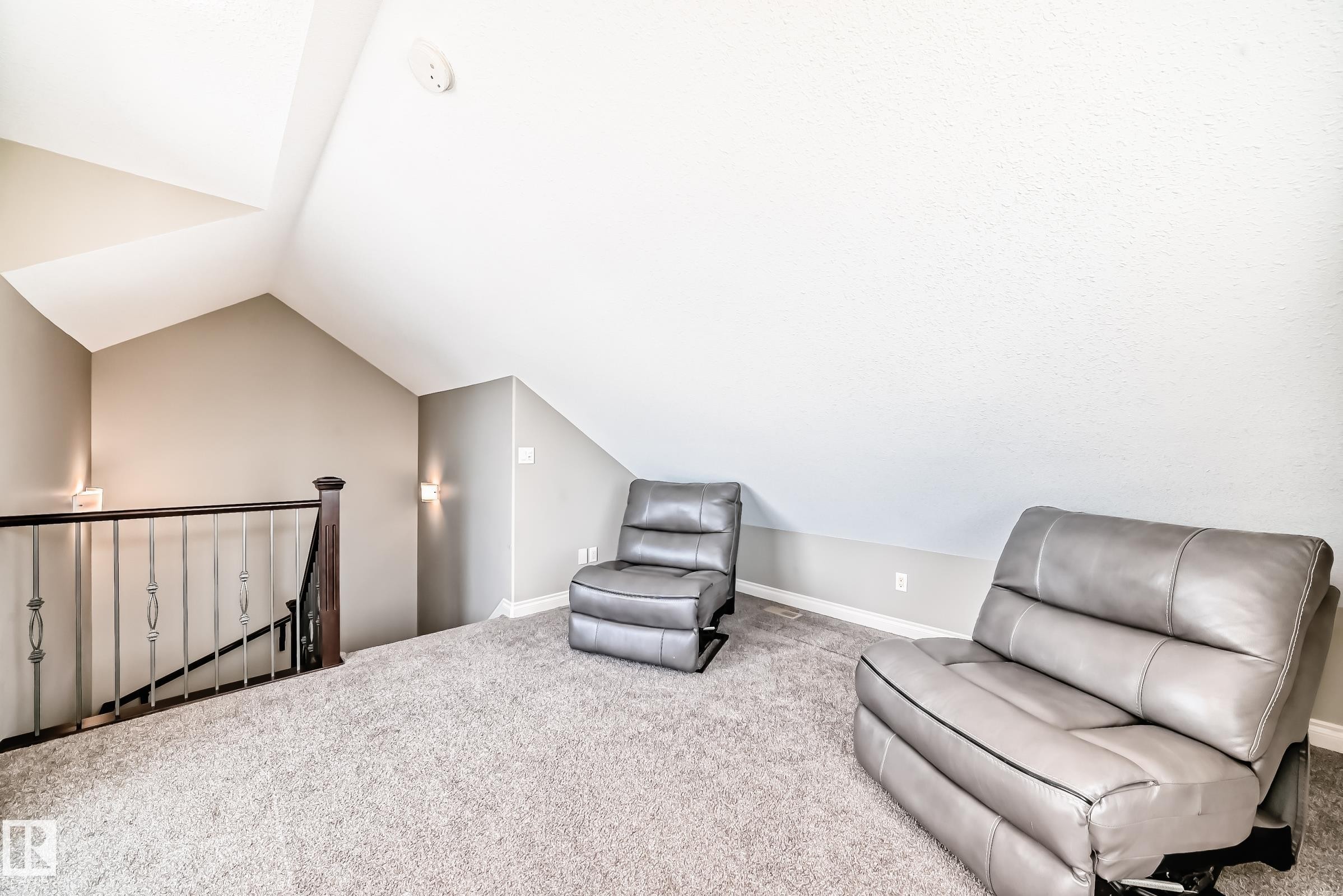 Carpeted loft area featuring vaulted ceilings, light neutral wall paint, and a dark wood and wrought iron staircase railing - 10519 114 Avenue, Edmonton, AB - Indoor