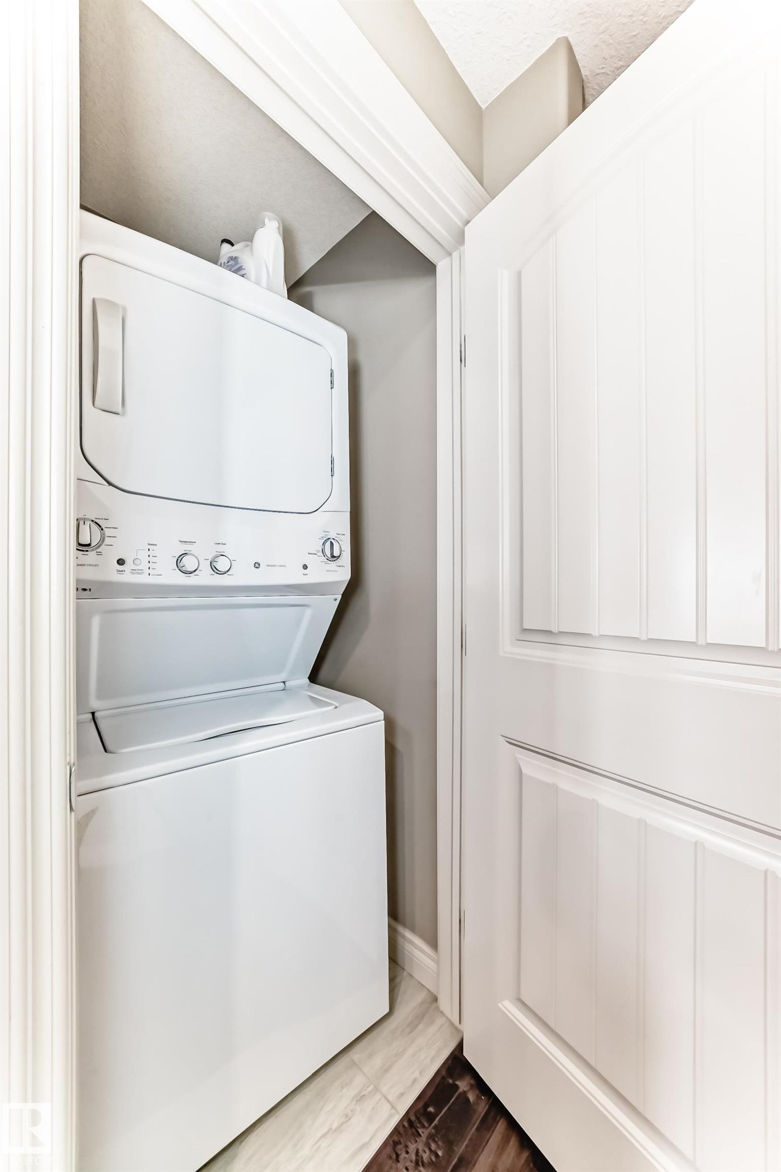 White stacked washer and dryer unit within a dedicated closet space, featuring neutral wall paint and white trim - 10519 114 Avenue, Edmonton, AB - Indoor Photo Showing Laundry Room