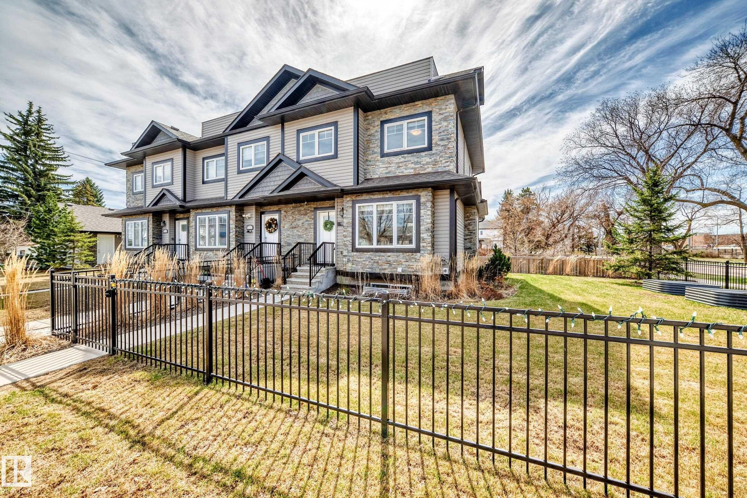 Modern multi-level townhome featuring stone and siding exterior, multiple gables, individual front entrances with covered stoops, and a black wrought iron fence enclosing the front yard - 10519 114 Avenue, Edmonton, AB - Outdoor With Facade