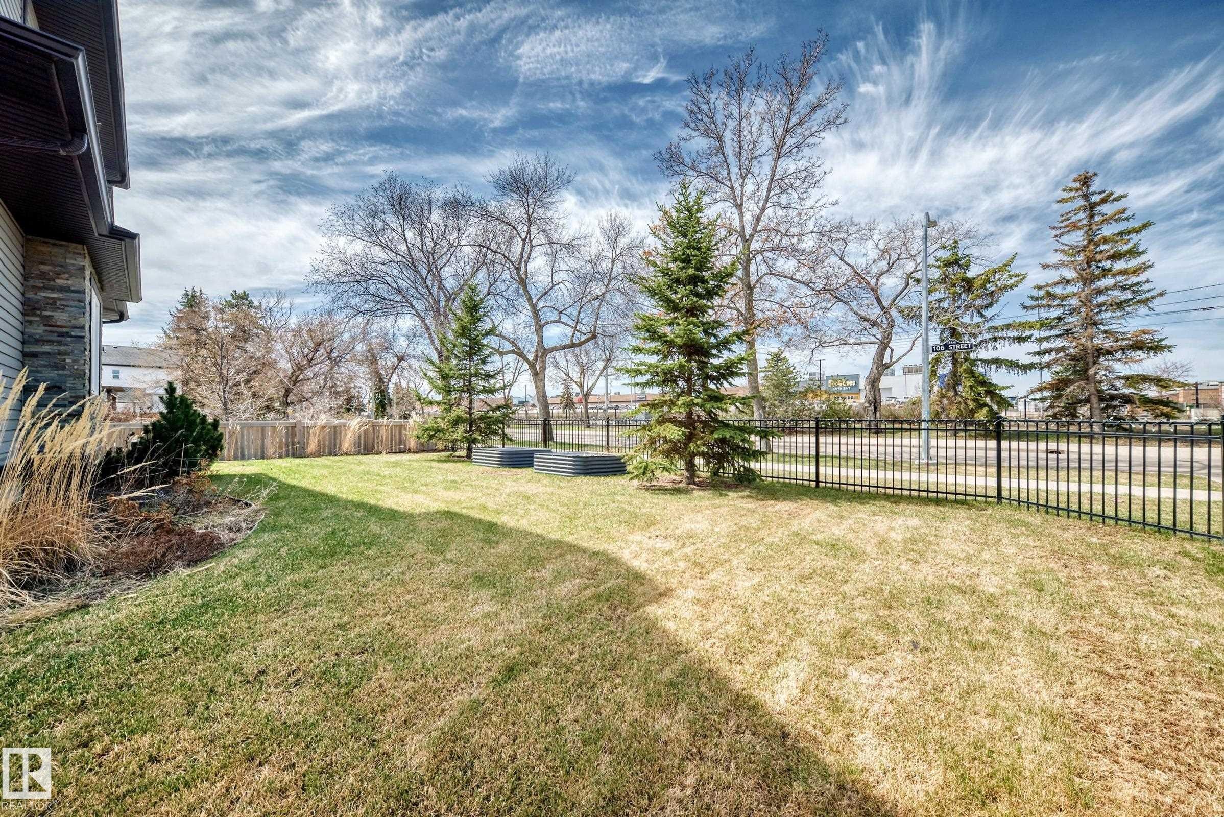 Expansive yard featuring a manicured lawn, mature trees, and a black metal fence - 10519 114 Avenue, Edmonton, AB - Outdoor