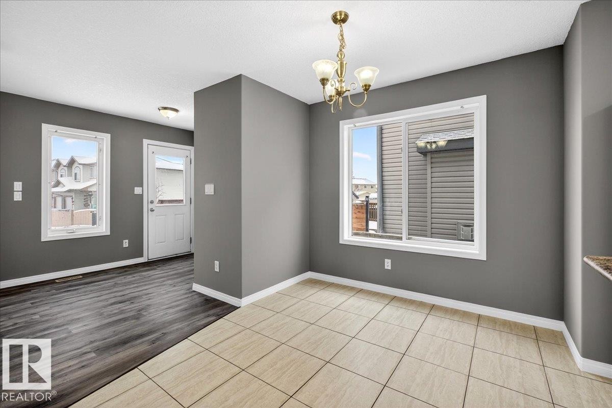 Unfurnished dining area with a chandelier, healthy amount of natural light, a textured ceiling, and light wood-style floors - 150 Acacia Circle, Leduc, AB - Indoor Photo Showing Other Room