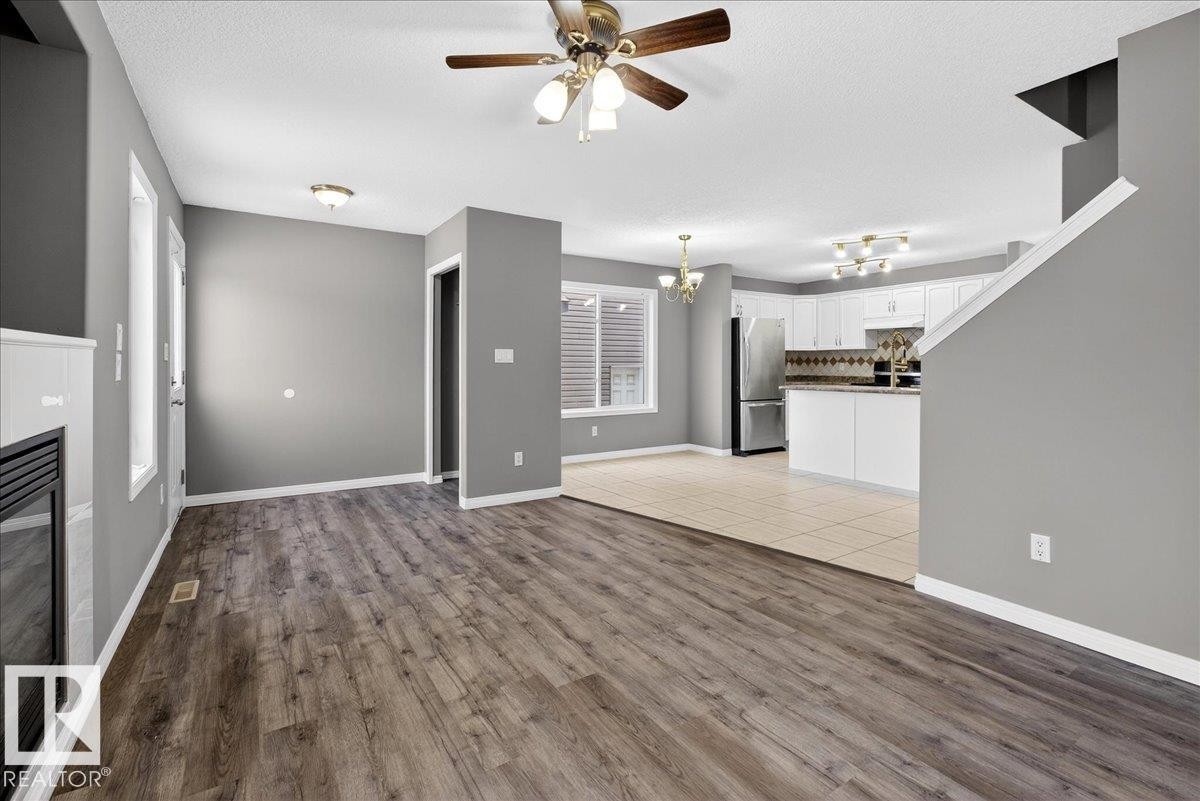 Unfurnished living room featuring light wood finished floors, a chandelier, a textured ceiling, and a ceiling fan - 150 Acacia Circle, Leduc, AB - Indoor Photo Showing Other Room With Fireplace