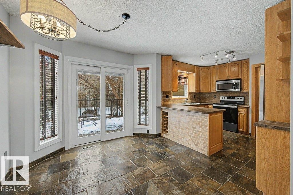 The kitchen and dining area features natural stone floor tiles, wood cabinetry, and a kitchen island with a brick-style facade and integrated wine storage - Edmonton, AB - Indoor Photo Showing Kitchen
