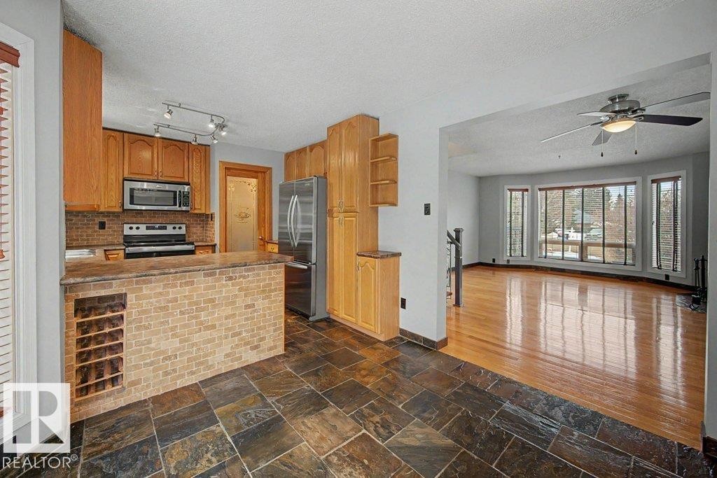 Kitchen featuring wood cabinetry, stainless steel appliances, a brick-style island with built-in wine storage, and slate tile flooring - Edmonton, AB - Indoor