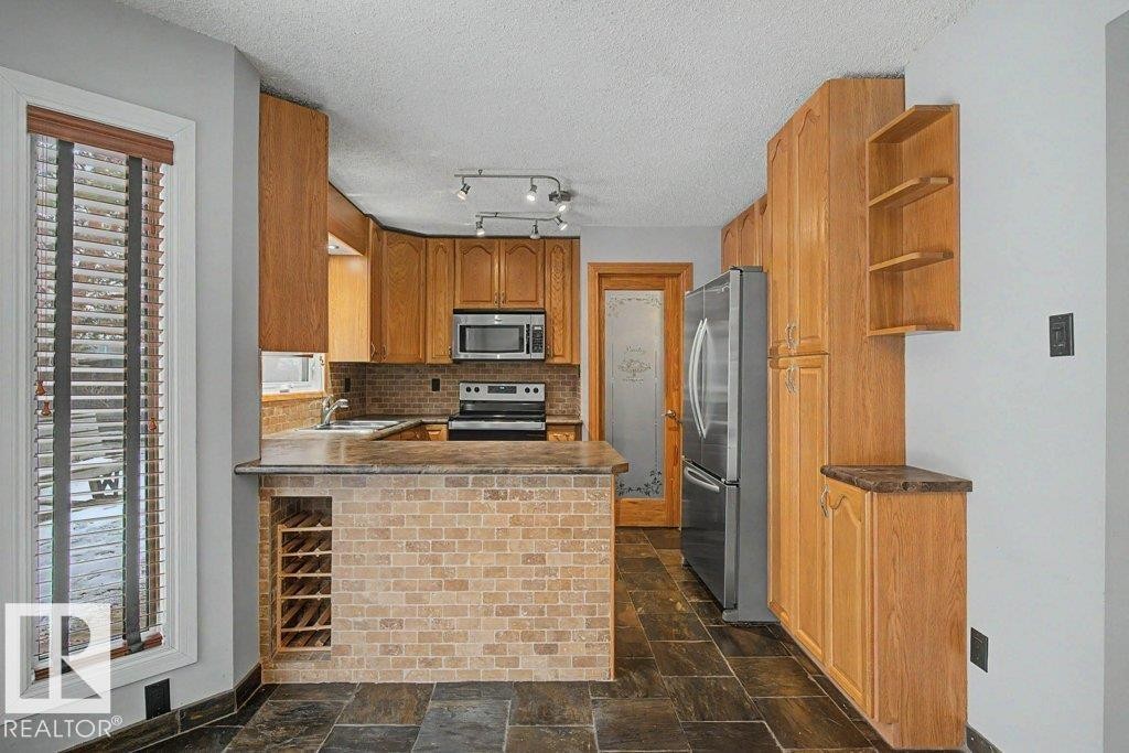 The kitchen features extensive wood cabinetry, a brick-textured island with integrated wine storage, and dark tile flooring - Edmonton, AB - Indoor Photo Showing Kitchen
