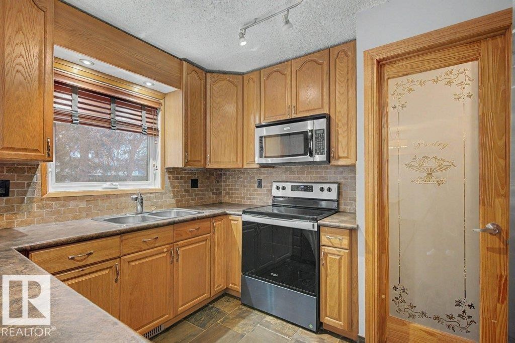 The kitchen features light wood cabinetry, a double basin sink, and a stainless steel over-the-range microwave and electric stove - Edmonton, AB - Indoor Photo Showing Kitchen With Double Sink