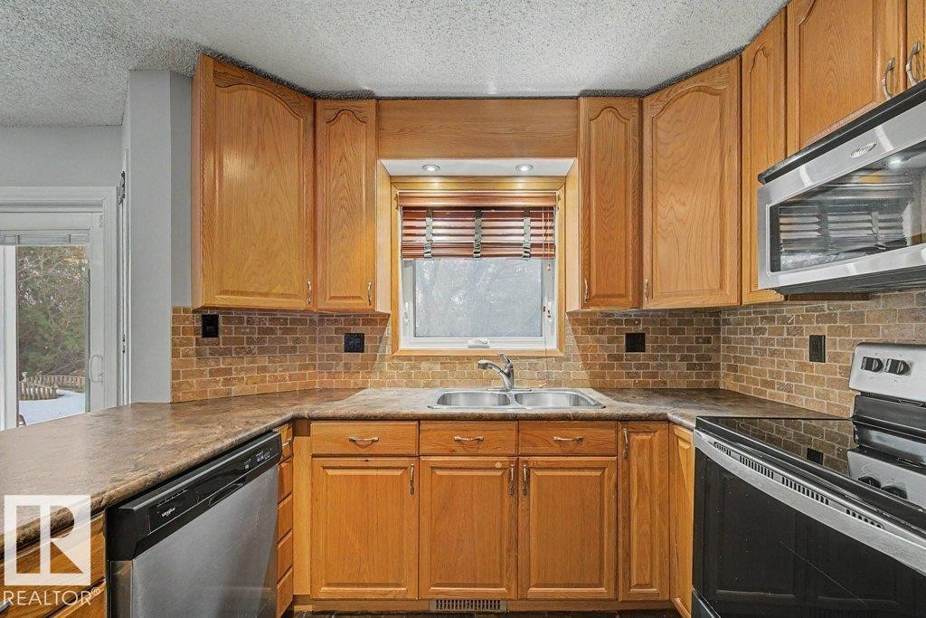 Well-appointed kitchen featuring wood cabinetry, a double basin sink, and stainless steel appliances including a dishwasher, microwave, and electric range - Edmonton, AB - Indoor Photo Showing Kitchen With Double Sink