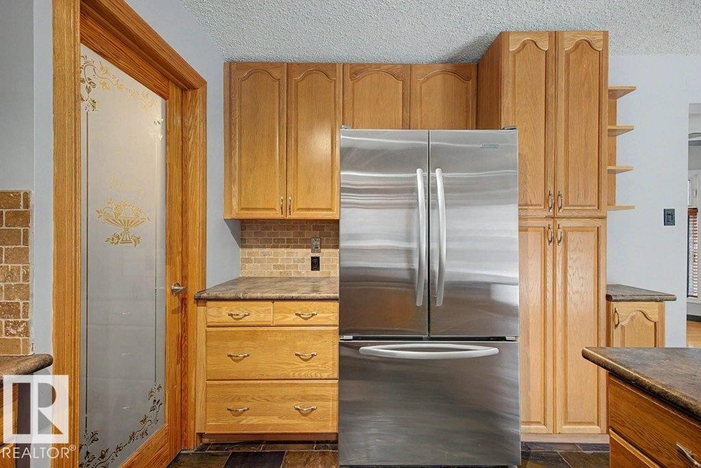 The kitchen features wooden cabinetry, a tiled backsplash, and a stainless steel refrigerator - Edmonton, AB - Indoor Photo Showing Kitchen