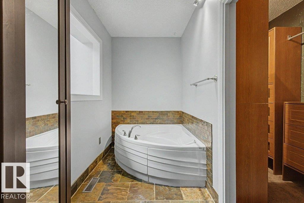 This bathroom features a corner soaking tub with a tiled surround, a window providing natural light, and tiled flooring - Edmonton, AB - Indoor