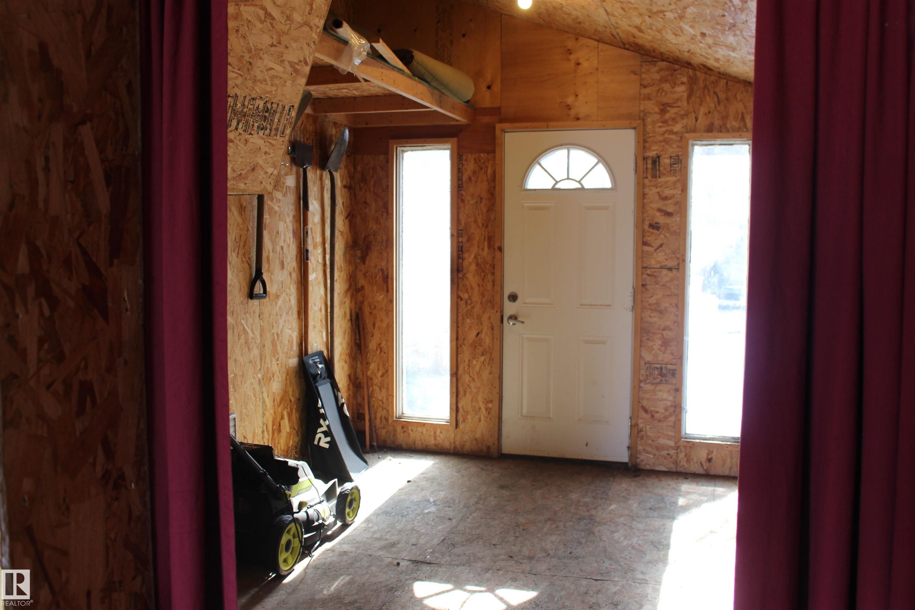 The interior space features wood paneling, a white entry door with an arched window, and two tall windows providing natural light - Edmonton, AB - Indoor Photo Showing Other Room