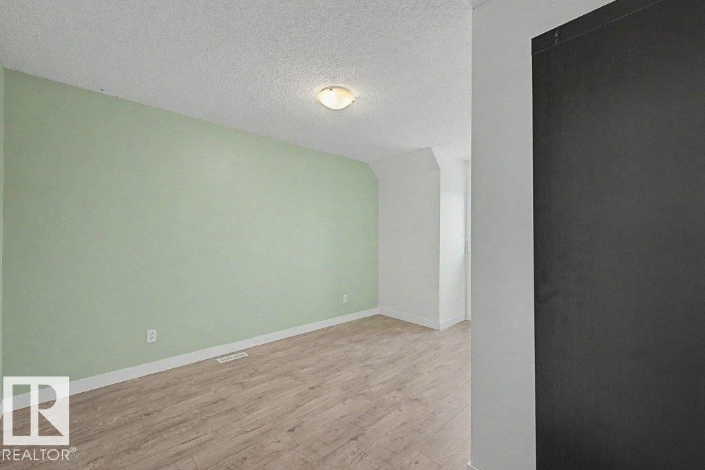 The property features light wood-style flooring, light green walls, and white trim throughout the space - Edmonton, AB - Indoor Photo Showing Other Room