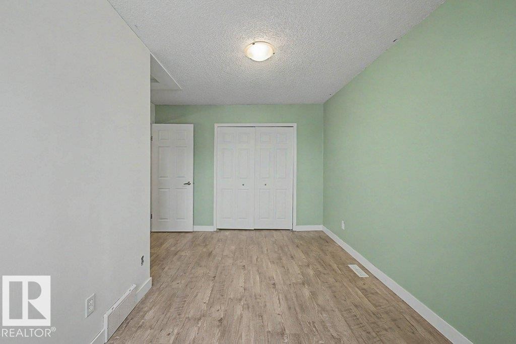 This room features light green walls, wood-style flooring, a white door, and a closet with white bi-fold doors - Edmonton, AB - Indoor Photo Showing Other Room