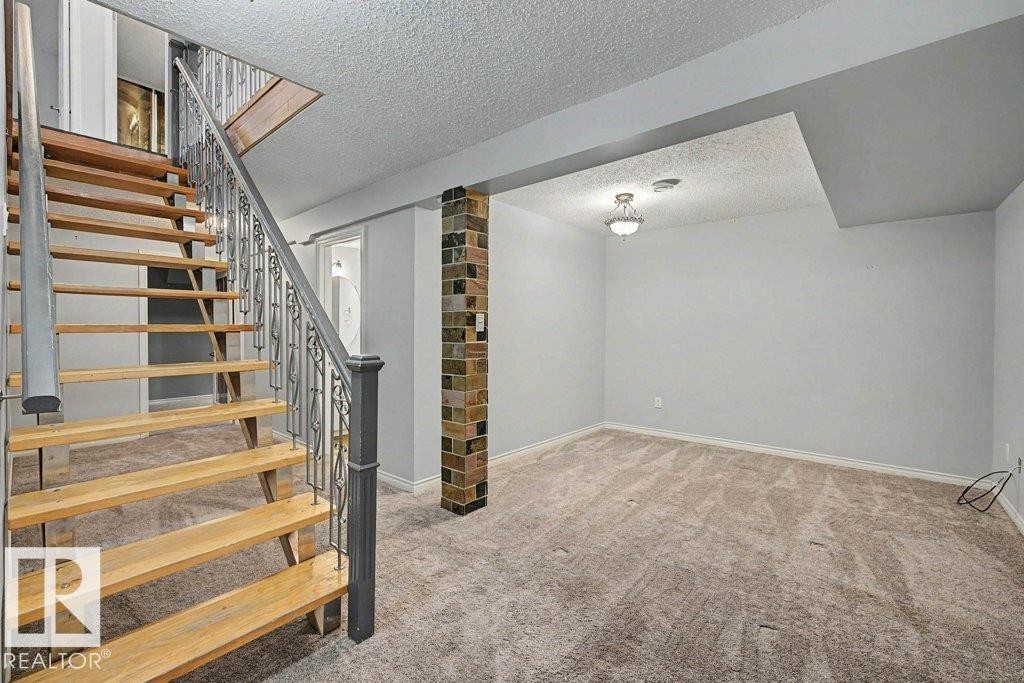 Spacious room featuring light-colored carpet, a ceiling light fixture, and a decorative brick column - Edmonton, AB - Indoor Photo Showing Other Room