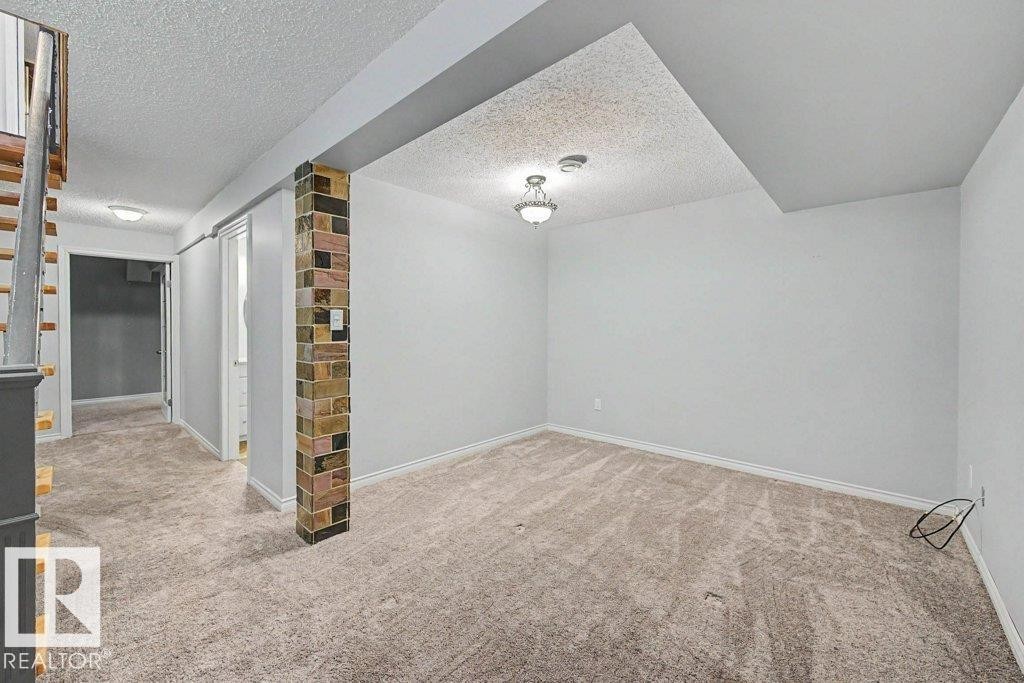 Inviting space featuring light-colored carpeting, white walls, and a decorative brick column - Edmonton, AB - Indoor Photo Showing Other Room