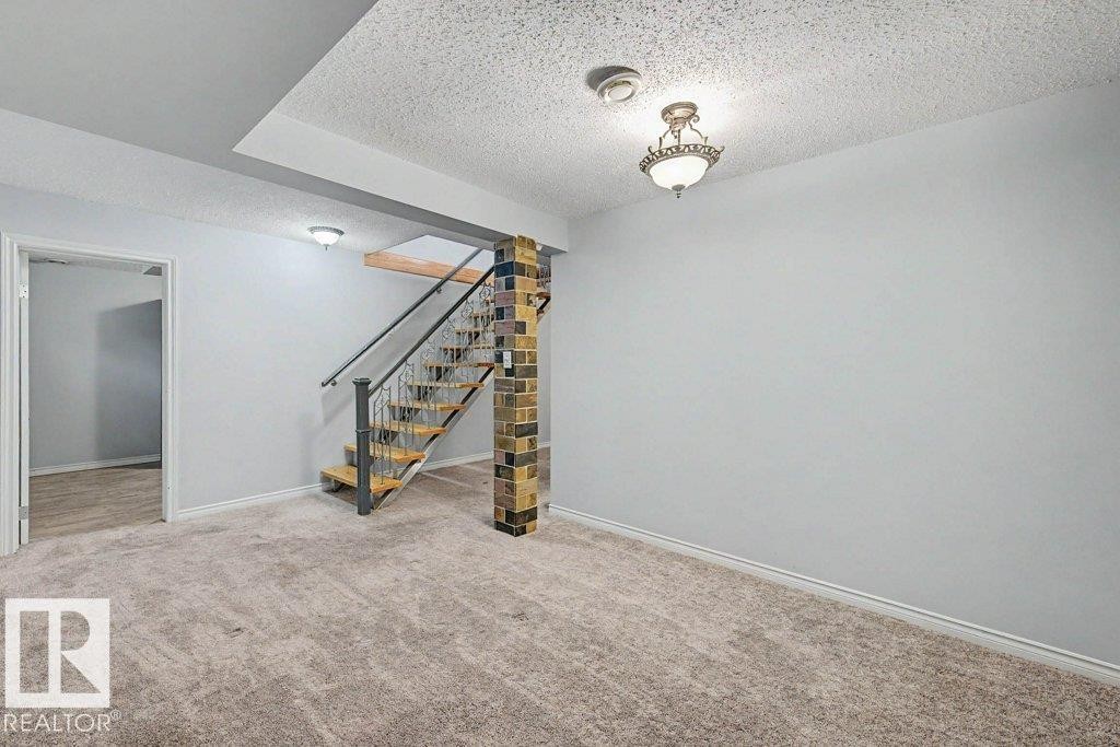 Spacious room featuring carpeting, light-colored walls, and a staircase with an ornamental railing - Edmonton, AB - Indoor Photo Showing Other Room