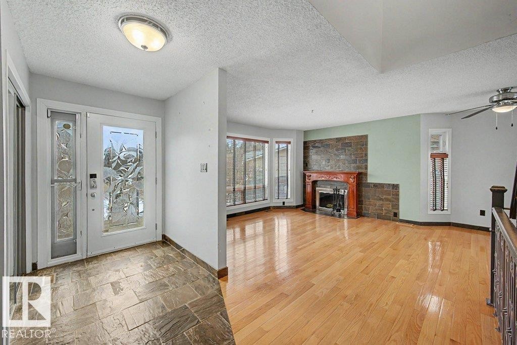Inviting entry with stone tile flooring leading to a living area featuring hardwood floors, a stone accent wall, and a fireplace with a wood mantel - Edmonton, AB - Indoor With Fireplace