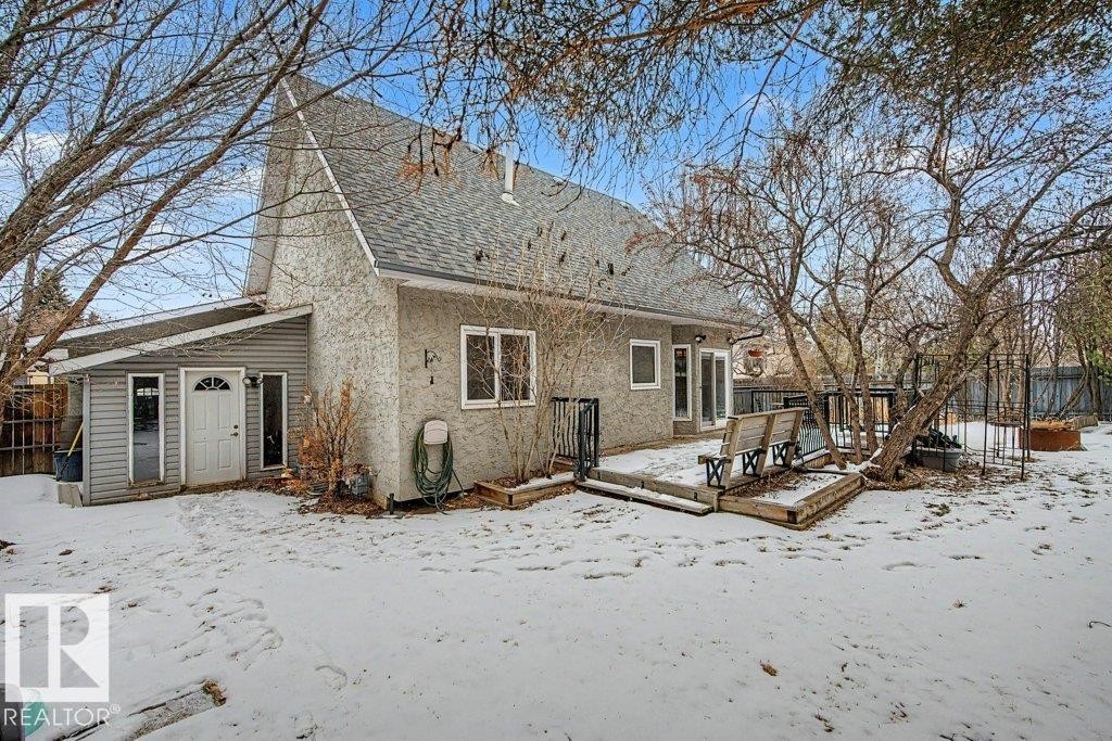 The property features a sloped roof and a rear deck with built-in benches, set within a yard that includes several mature trees - Edmonton, AB - Outdoor With Deck Patio Veranda