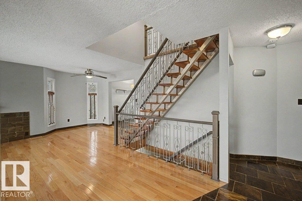 This space features hardwood flooring and a stylish open staircase with decorative metal railings - Edmonton, AB - Indoor Photo Showing Other Room