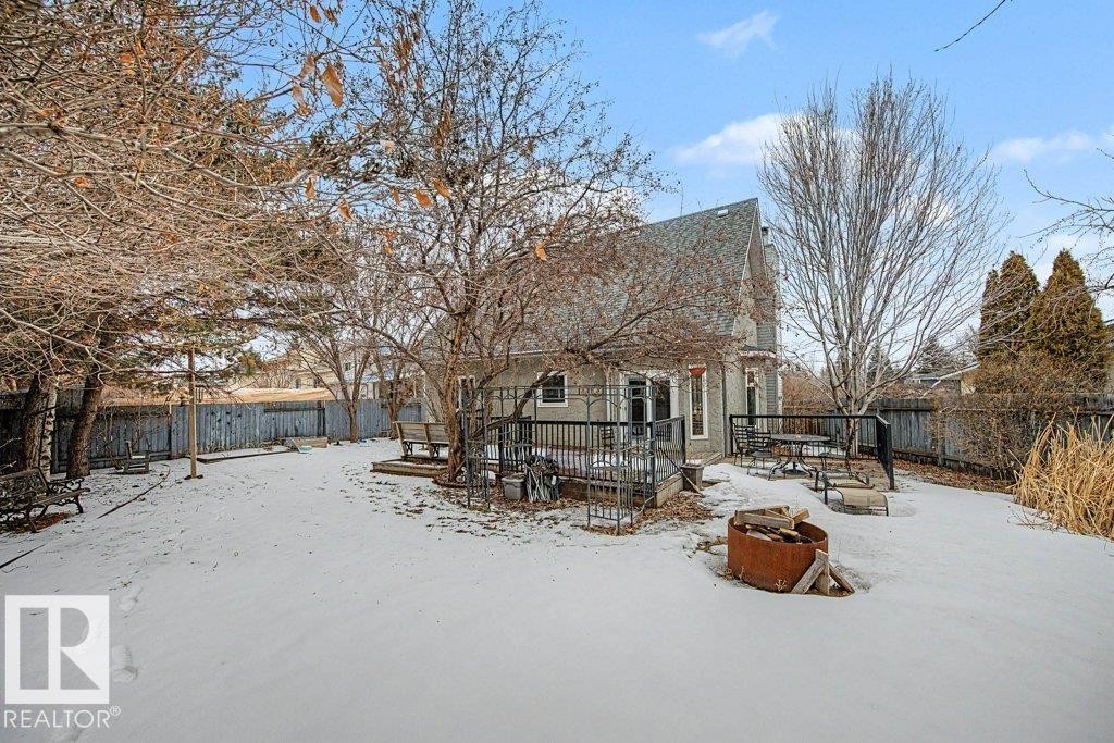 The property features a fenced backyard with a snow-covered lawn, mature trees, and a ground-level deck - Edmonton, AB - Outdoor