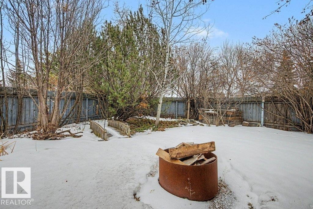 The property features a fenced yard with a fire pit, a small wooden bridge, and a mix of deciduous and evergreen trees - Edmonton, AB - Outdoor