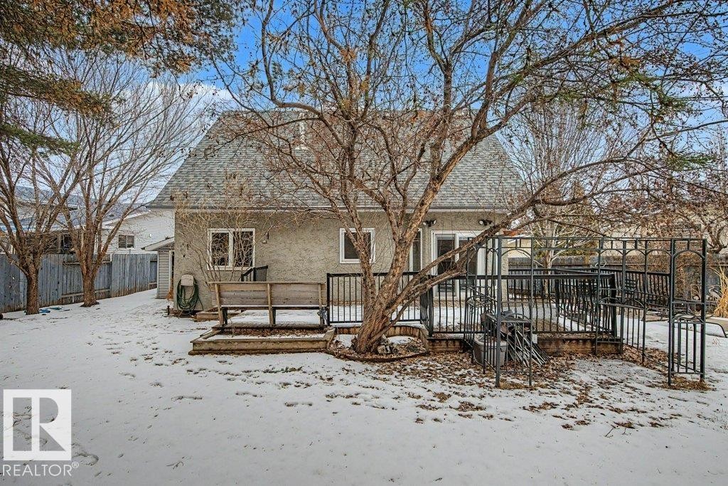 The property features a spacious backyard with a deck and a black metal fence, complemented by mature trees and a shingled roof - Edmonton, AB - Outdoor With Deck Patio Veranda