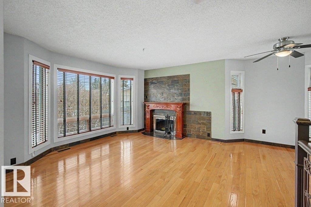 Living area featuring hardwood floors, a stone-clad fireplace with a decorative mantel, and a bay window providing natural light - Edmonton, AB - Indoor Photo Showing Living Room With Fireplace