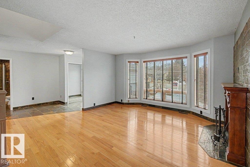 Living area featuring hardwood flooring, a fireplace with a stone surround and wood mantel, and large windows with blinds - Edmonton, AB - Indoor Photo Showing Other Room