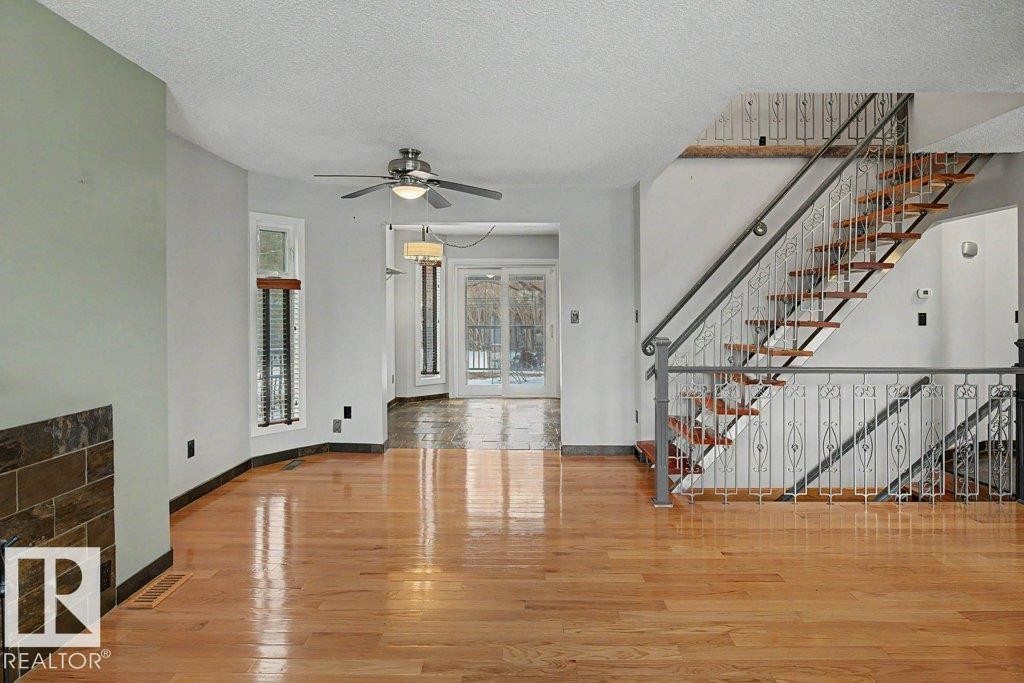 The interior features hardwood flooring, a ceiling fan, and a staircase with a decorative metal railing - Edmonton, AB - Indoor Photo Showing Other Room