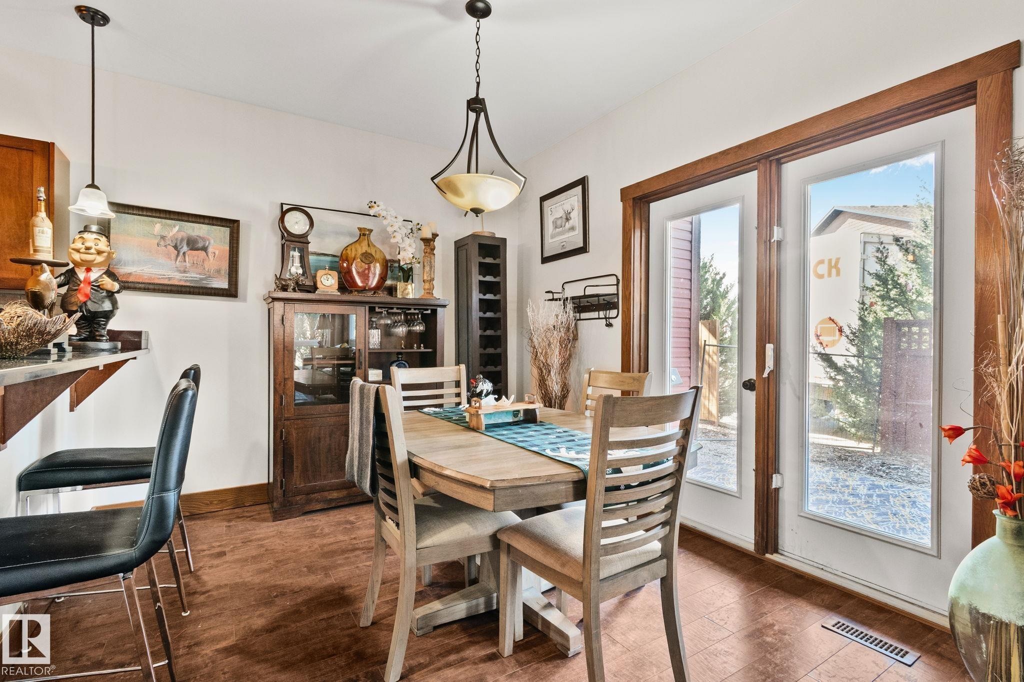 Dining area featuring wood-finish flooring, a pendant light fixture, and double glass-paneled doors with wood trim - 2201 Graybriar Green, Stony Plain, AB - Indoor Photo Showing Dining Room