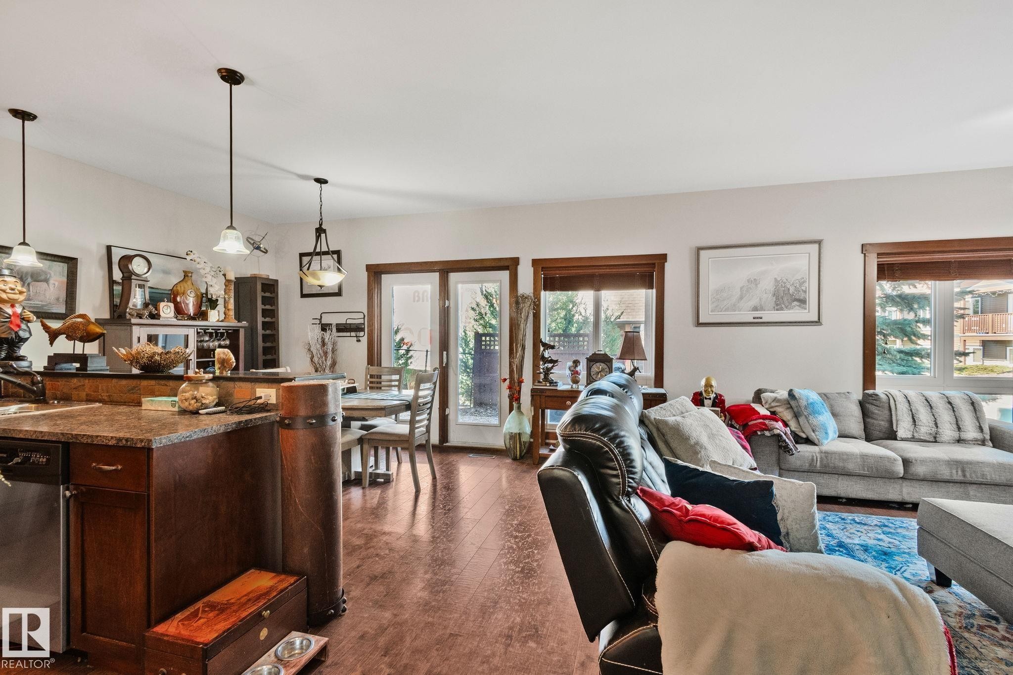 Open-concept living space featuring wood-finish flooring, a kitchen island with stone countertop, pendant lighting, and multiple windows with wood trim - 2201 Graybriar Green, Stony Plain, AB - Indoor Photo Showing Living Room