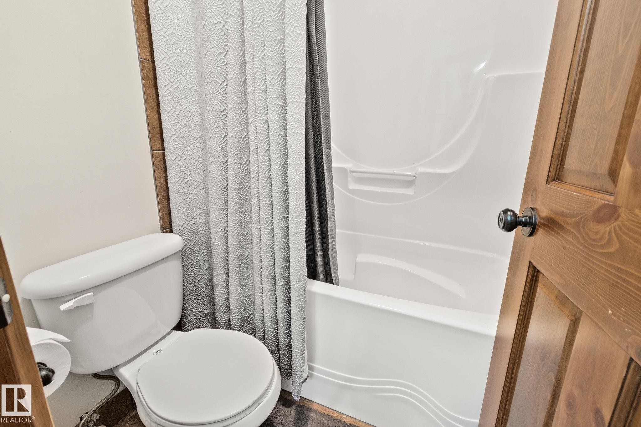 Bathroom featuring a white toilet, a shower/tub combination with a white surround, and a wood-paneled door - 2201 Graybriar Green, Stony Plain, AB - Indoor Photo Showing Bathroom
