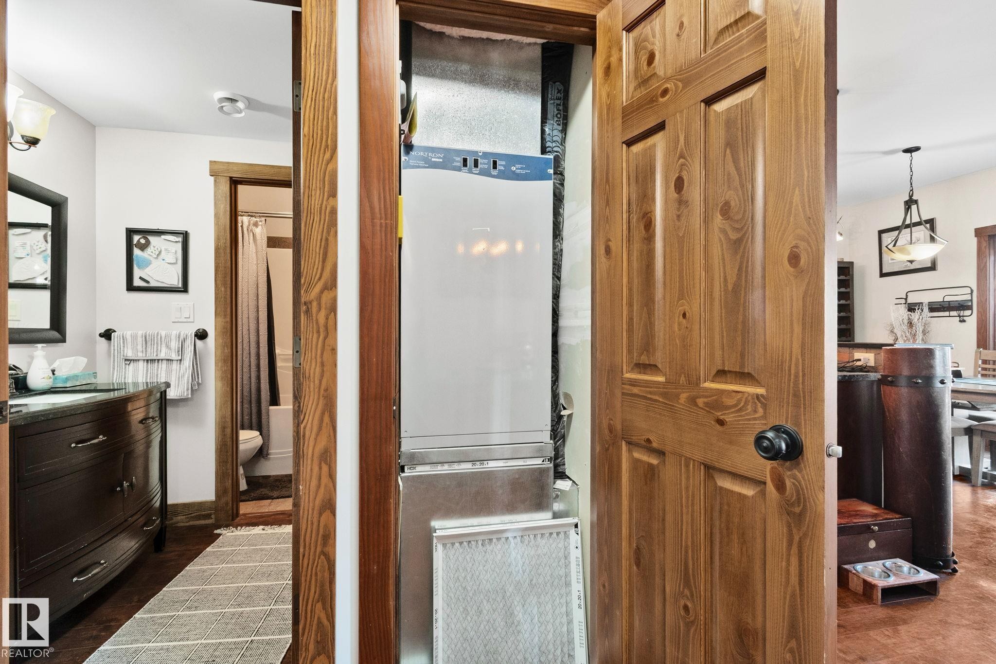Utility closet featuring a stacked appliance unit, wood-finish panel door, and dark hardware - 2201 Graybriar Green, Stony Plain, AB - Indoor