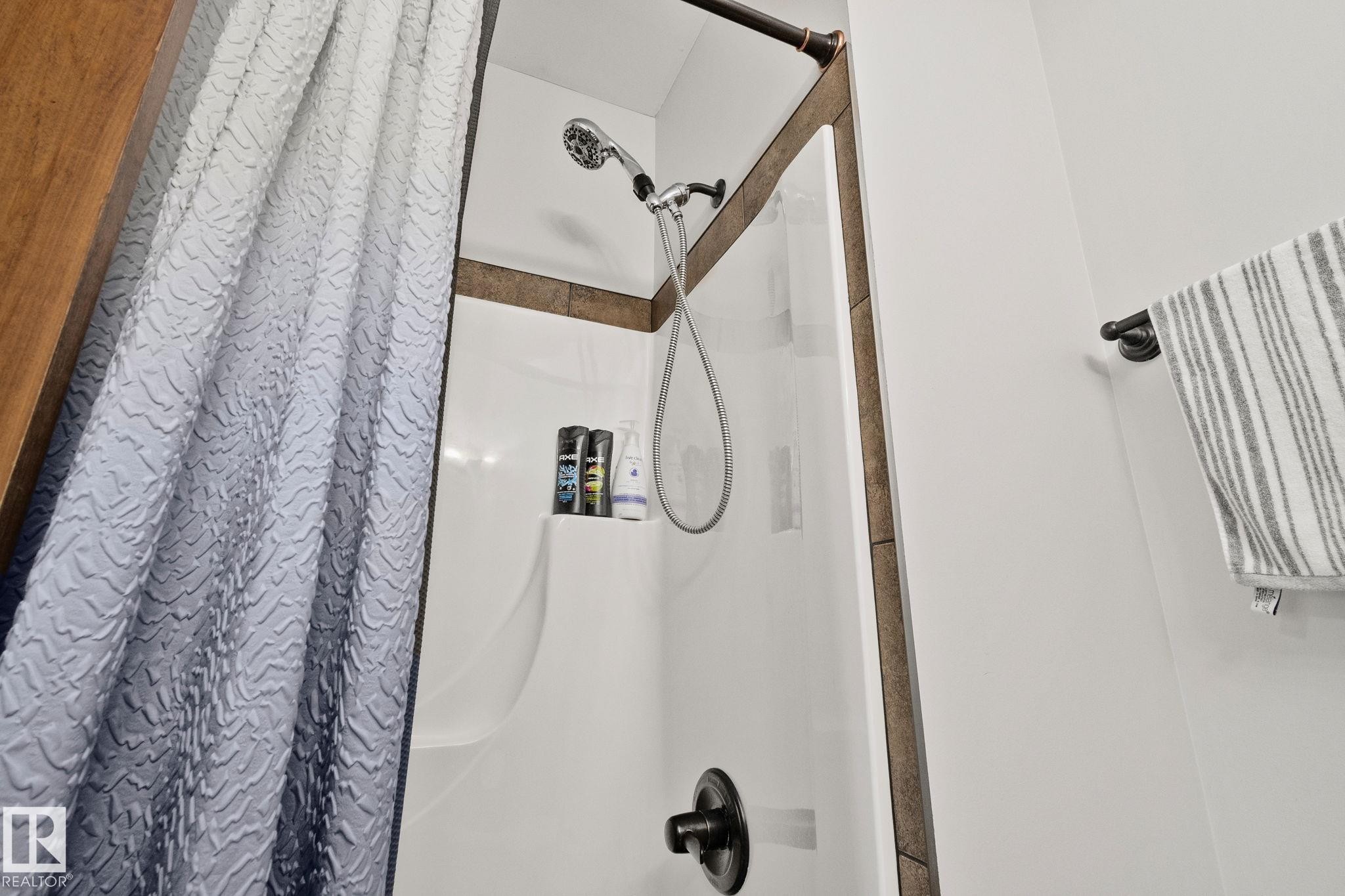 Shower enclosure featuring a built-in product shelf, handheld shower sprayer, dark bronze fixtures, and white wall paneling - 2201 Graybriar Green, Stony Plain, AB - Indoor Photo Showing Bathroom