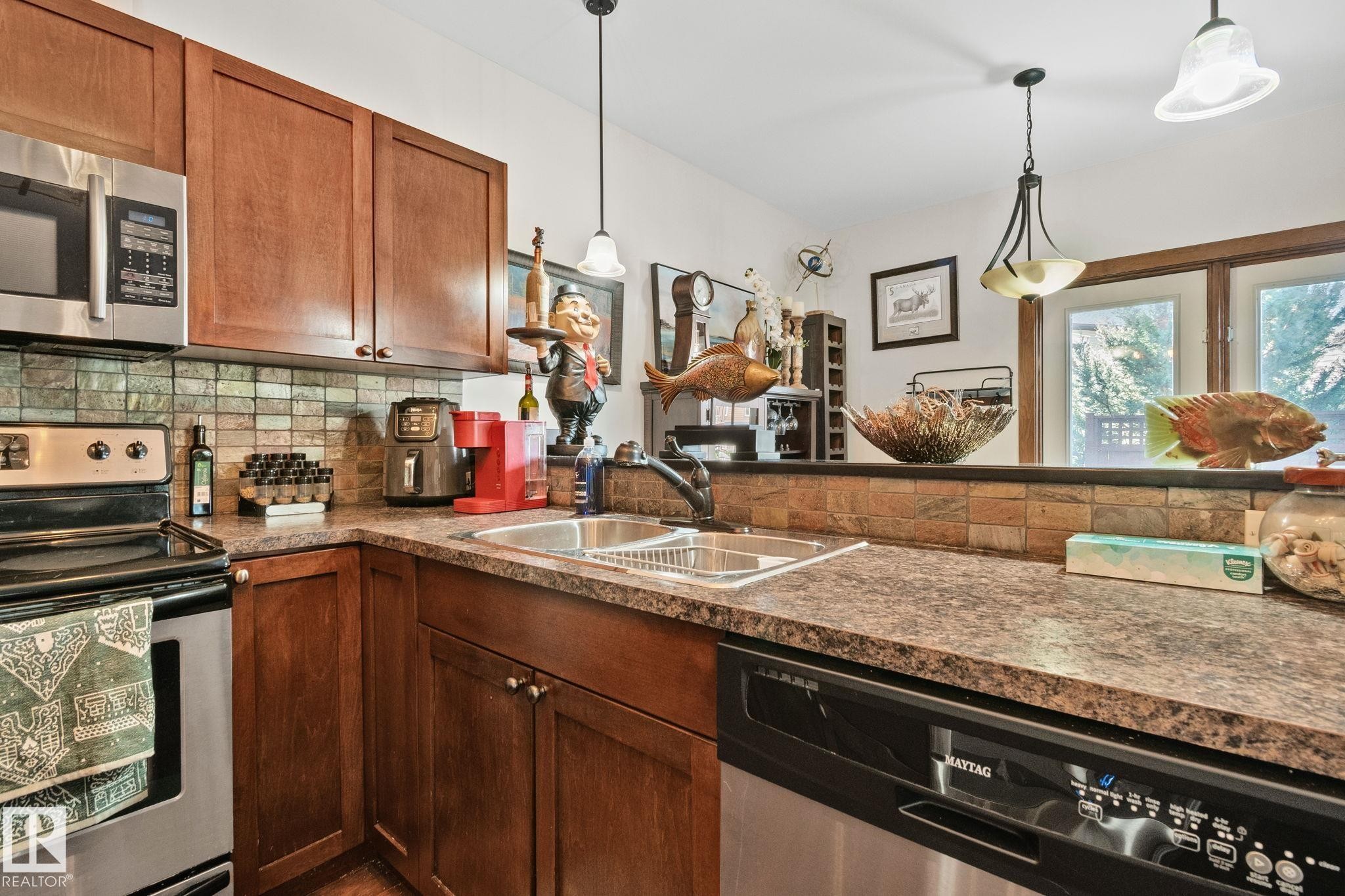 Kitchen featuring wood cabinetry, stainless steel microwave, stainless steel dishwasher, and a double basin stainless steel sink - 2201 Graybriar Green, Stony Plain, AB - Indoor Photo Showing Kitchen With Double Sink