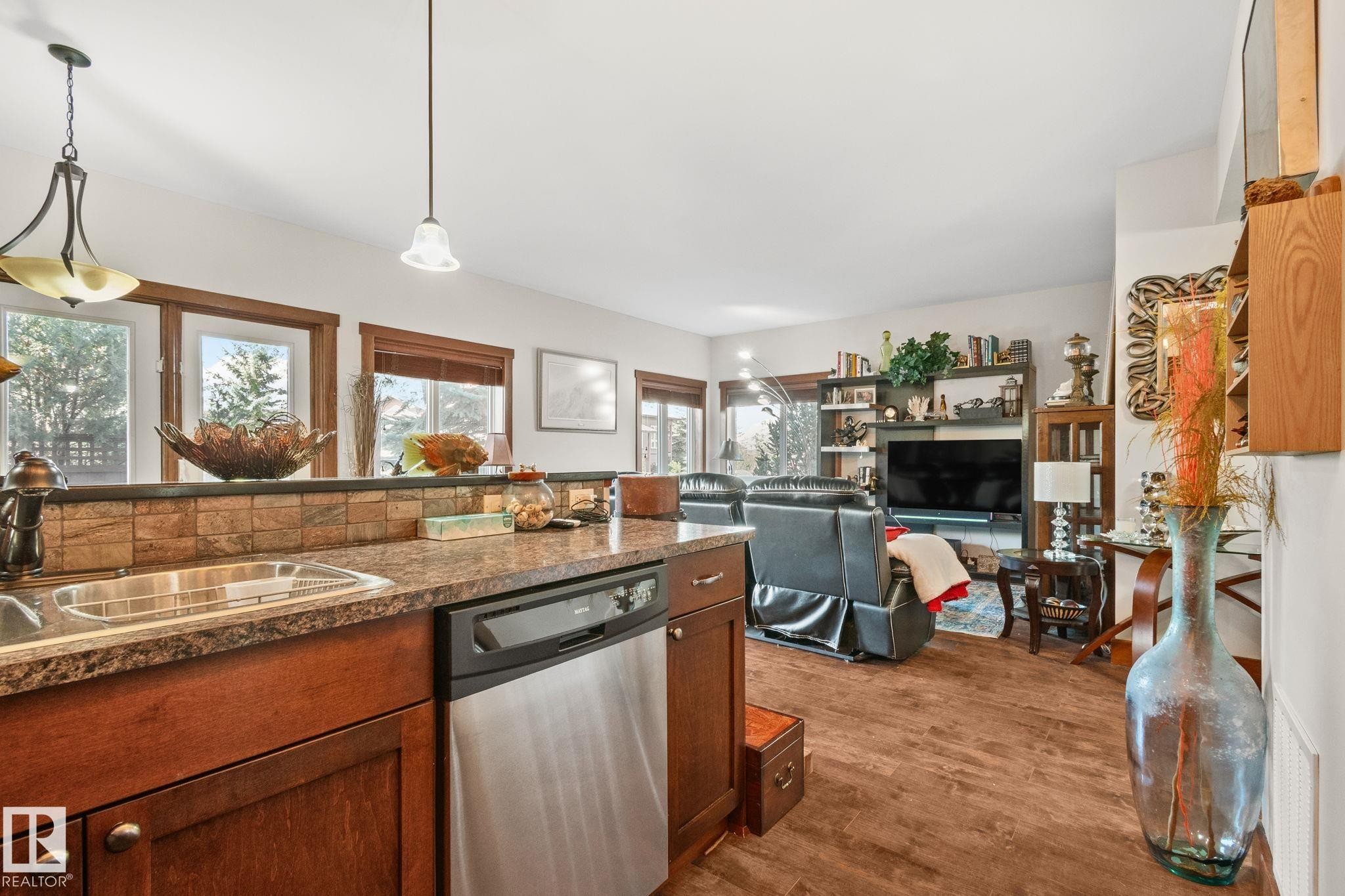 Kitchen featuring a stainless steel dishwasher, brown wood cabinetry, stone-finish countertops, and a tile backsplash - 2201 Graybriar Green, Stony Plain, AB - Indoor Photo Showing Kitchen With Double Sink