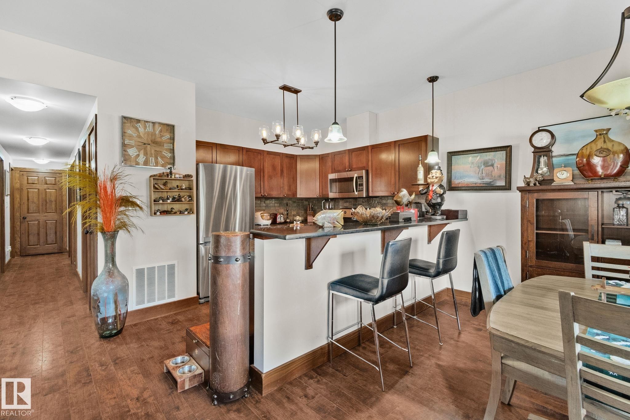 Kitchen and dining area featuring warm wood-finish flooring, rich wood cabinetry, stainless steel appliances, and a breakfast bar with pendant lighting - 2201 Graybriar Green, Stony Plain, AB - Indoor