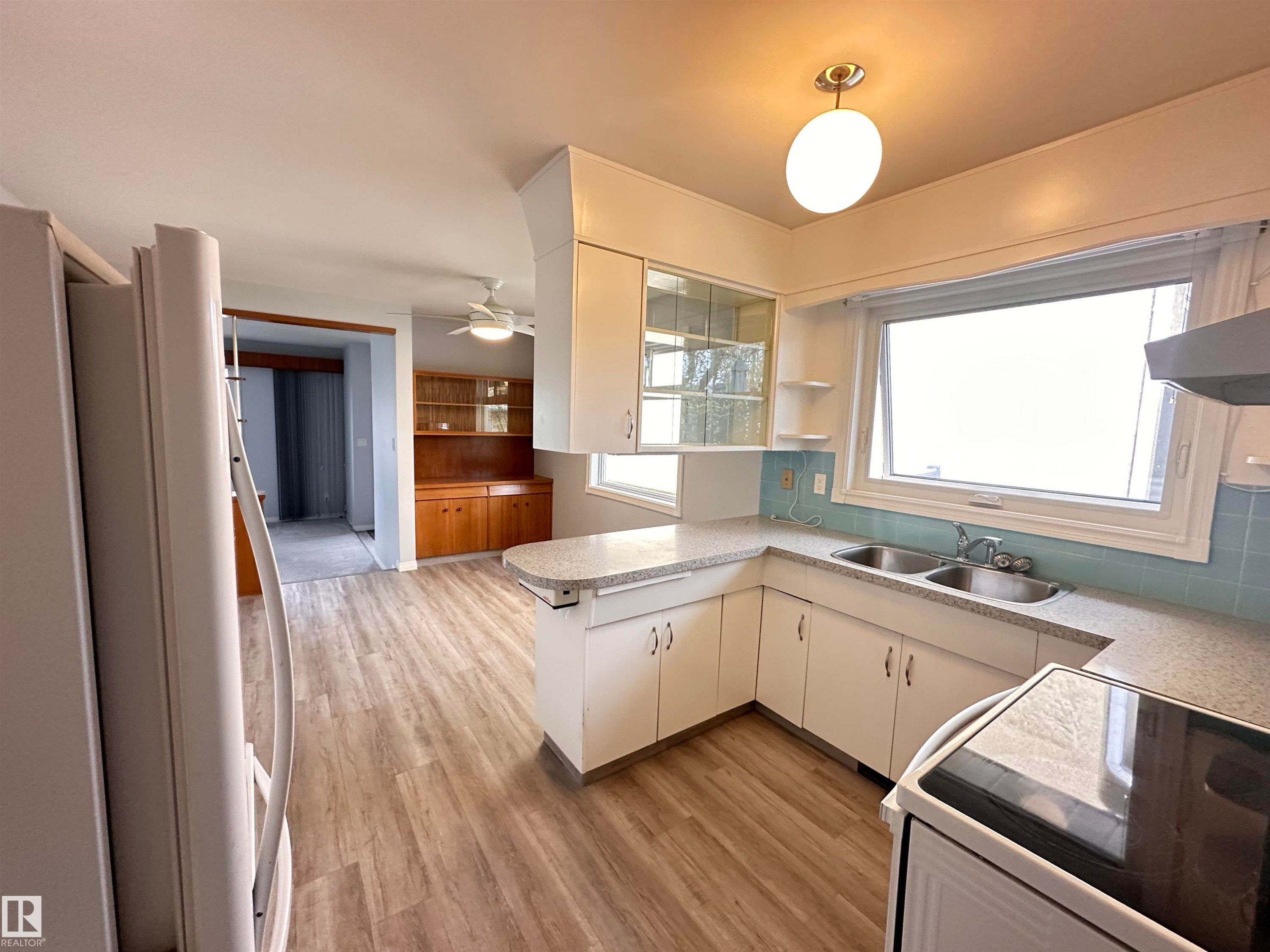 Kitchen featuring wood-finish flooring, white cabinetry, and light-colored countertops - 11131 52 Street, Edmonton, AB - Indoor Photo Showing Kitchen With Double Sink