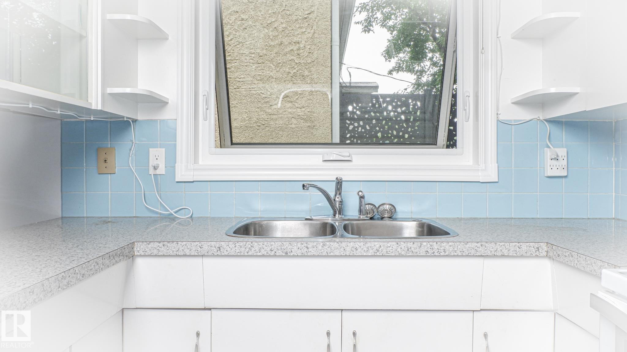 Kitchen area featuring a double-basin stainless steel sink, light blue tiled backsplash, and white cabinetry - 11131 52 Street, Edmonton, AB - Indoor Photo Showing Kitchen With Double Sink