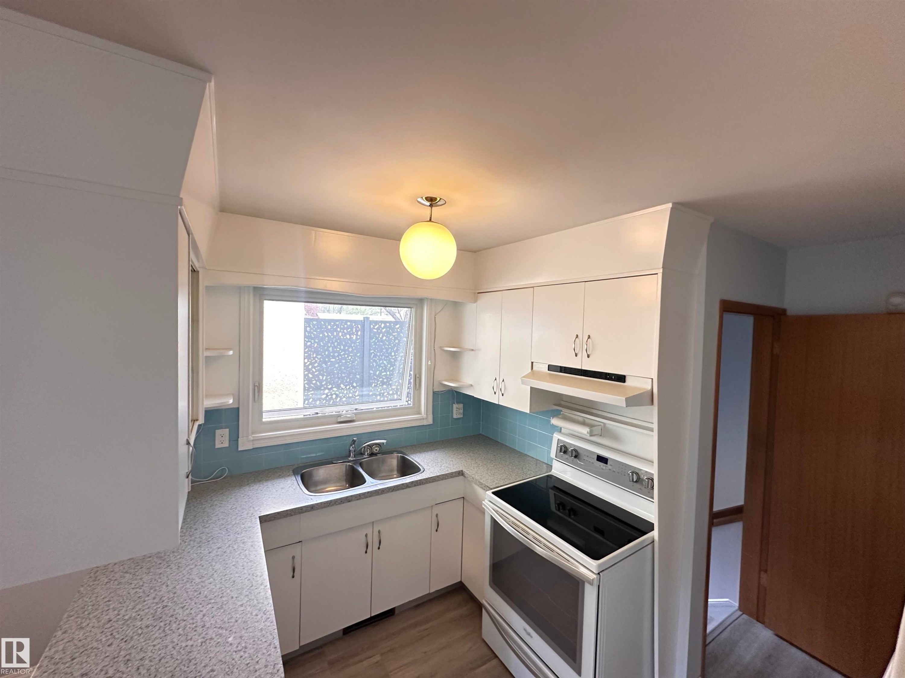 Kitchen featuring white cabinetry, light-toned countertops, a stainless steel double sink, a turquoise subway tile backsplash, and a white electric range - 11131 52 Street, Edmonton, AB - Indoor Photo Showing Kitchen With Double Sink